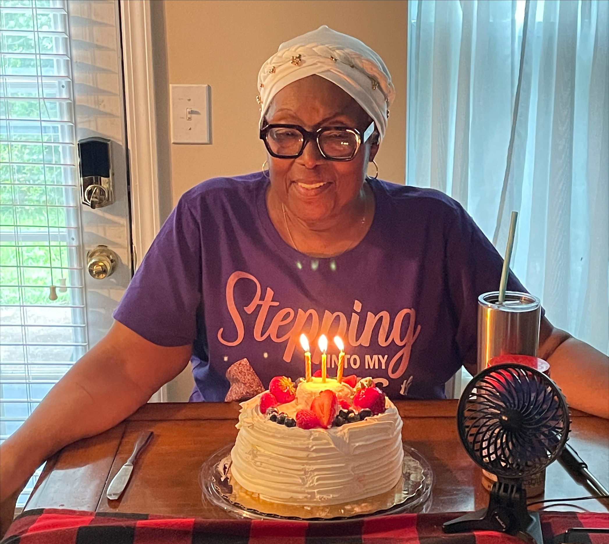 Eleasha's Nana with a small vanilla circle cake with candles. She is smiling and looking down at the cake.